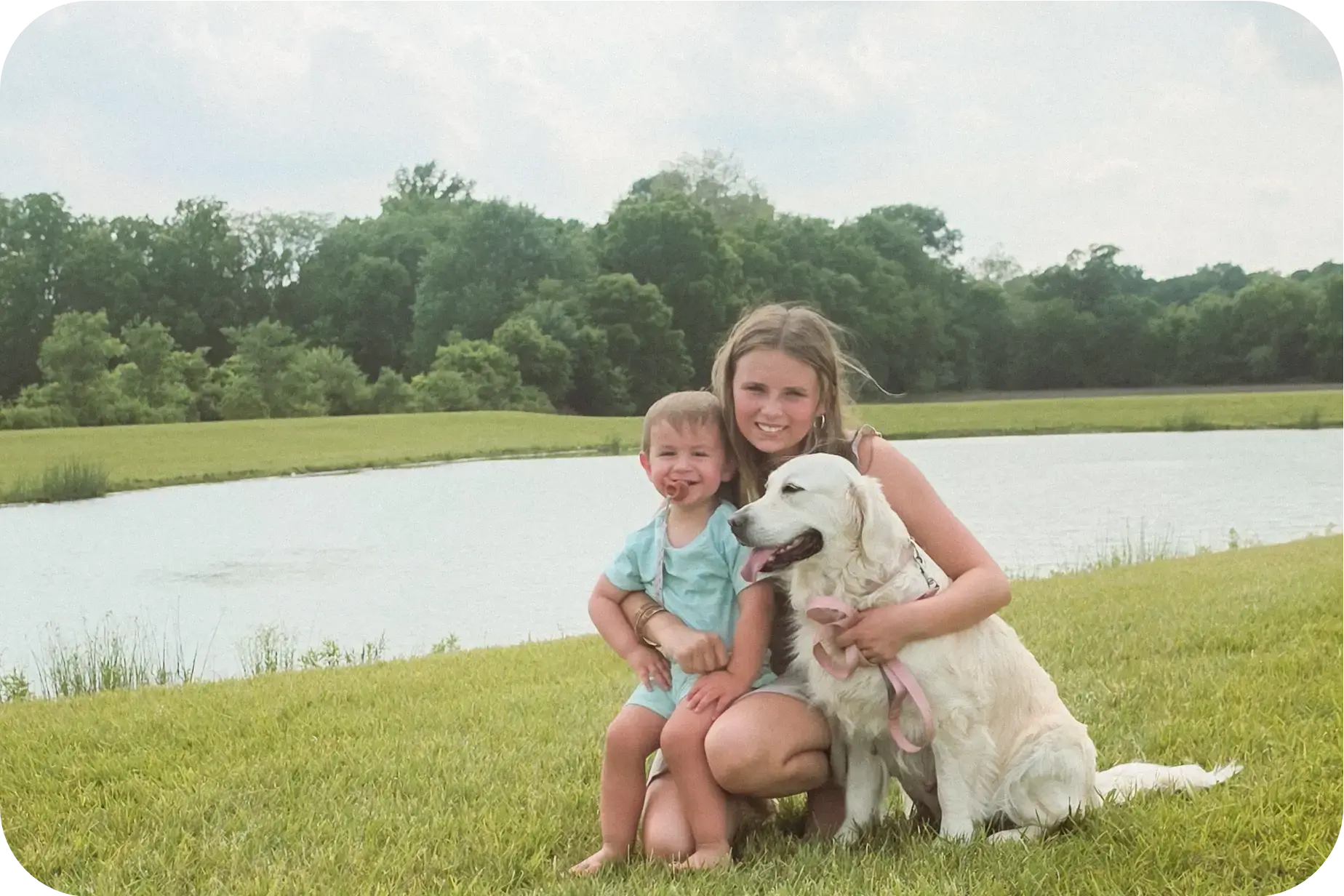 A child sitting with an English Cream Golden Retriever beside a pond